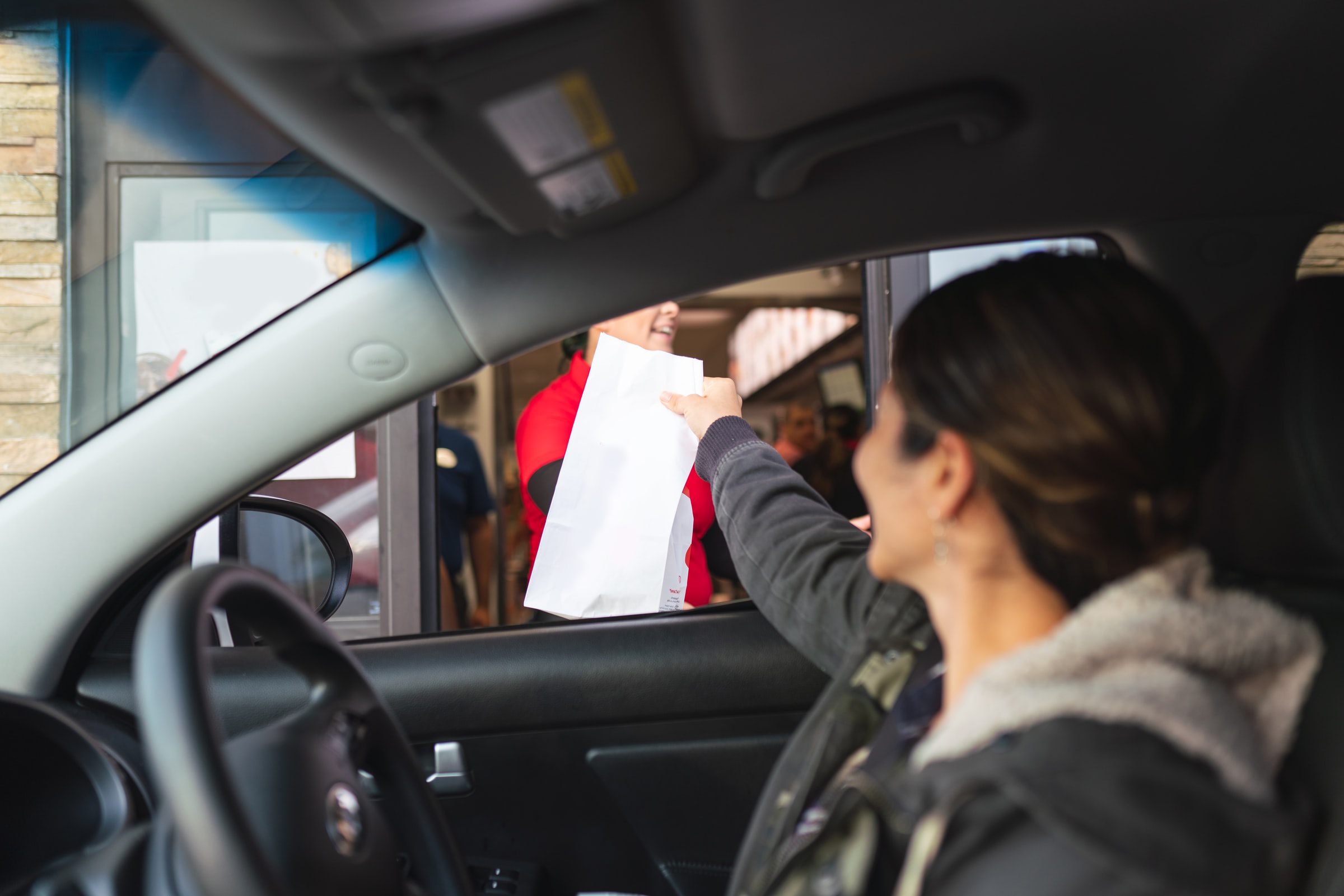 A person in a car taking a bag from a drive-thru window
